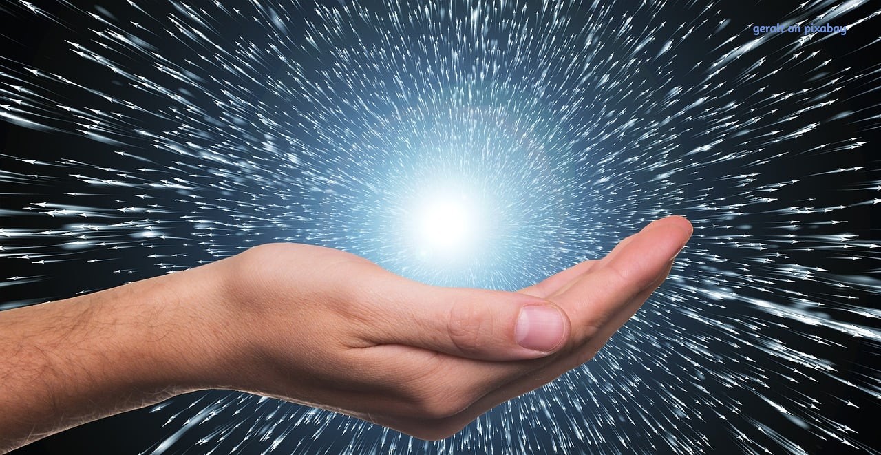 A human hand gently cupped upward, holding a radiant sphere of white light that radiates beams of energy outward, symbolizing healing energy and the flow of chakras.