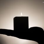 A silhouetted hand gently offering a lit candle against a soft, glowing background, symbolizing vulnerability, inner light, and the courage to hold oneself with tenderness.