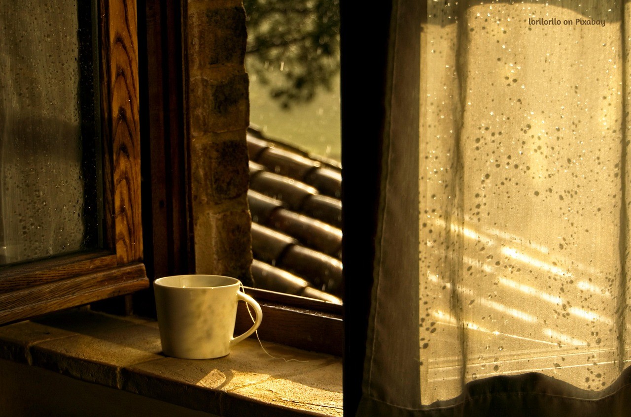 A white cup of tea resting on a sunlit windowsill, warm light filtering through rain-speckled glass, creating a quiet, contemplative scene.