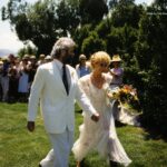 Lord Honey Bear and Lady Uppity walk hand in hand through the Buddha garden after exchanging their wedding vows on Lost Mesa, surrounded by family and framed by juniper trees on a bright summer day. Image by Thia Rose.