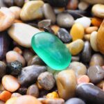 A bright green piece of sea glass standing out among smooth, multicolored beach stones.