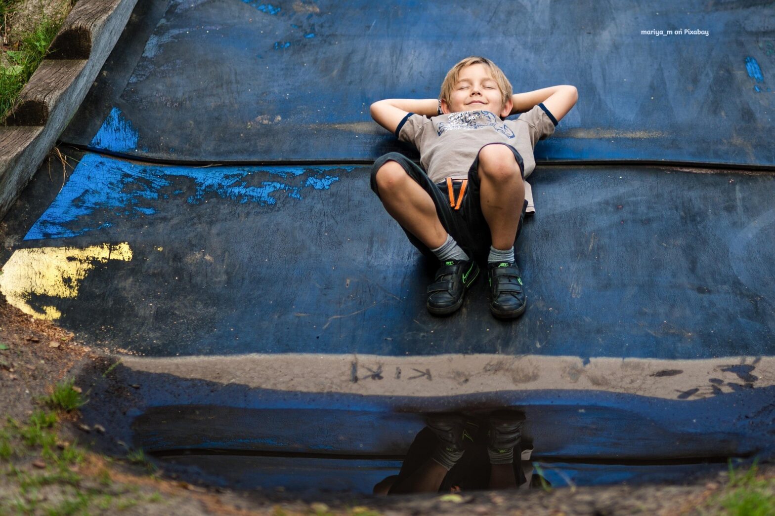 Feature image alt text: Happy boy relaxing on a slide with puddle reflection after rain. Image by mariya_m on Pixabay.